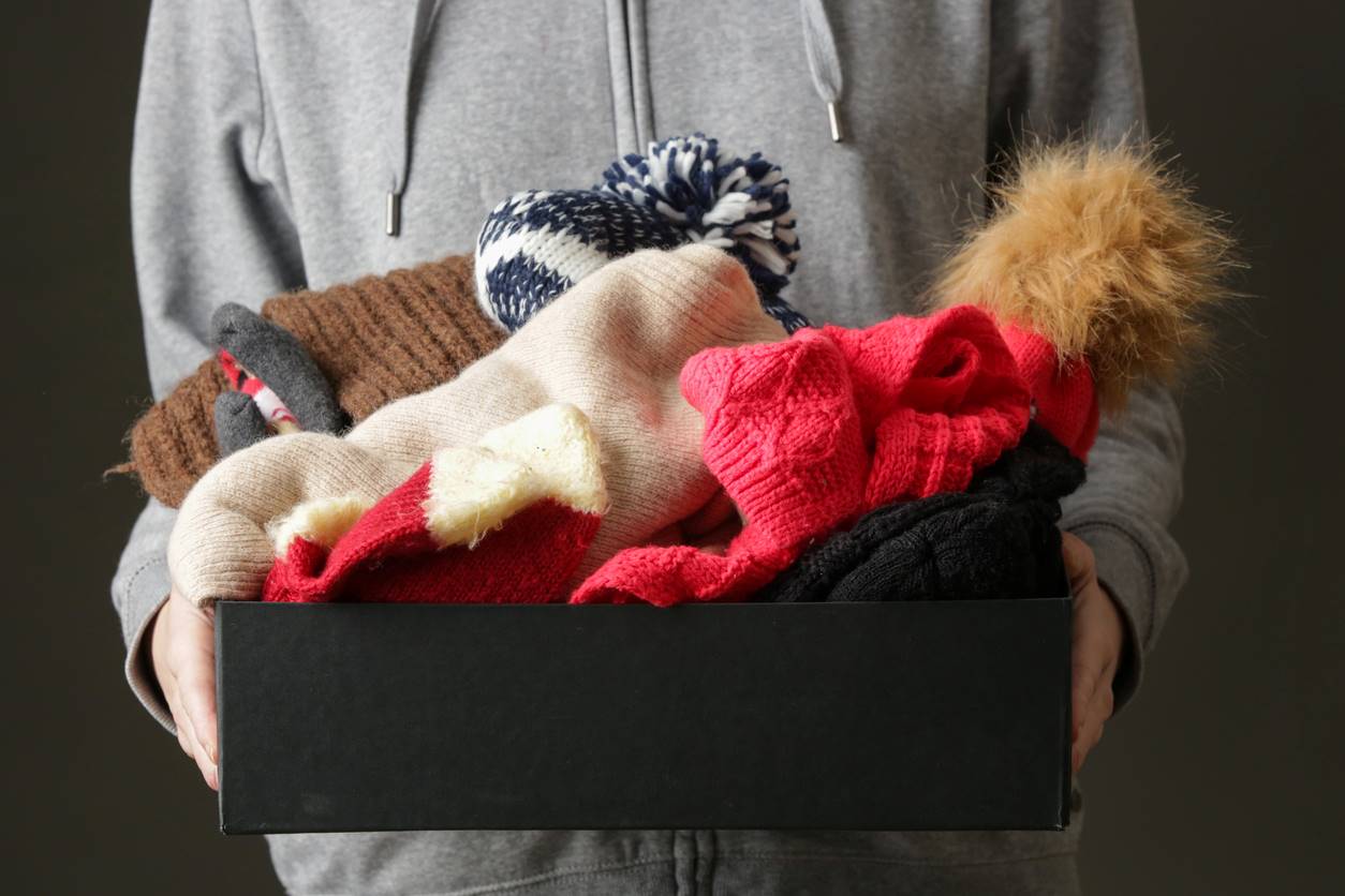 A person holding a small box full of winter hats and scarves
